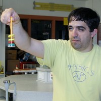Corey Mousseau demonstrating physics equipment in a classroom lab.